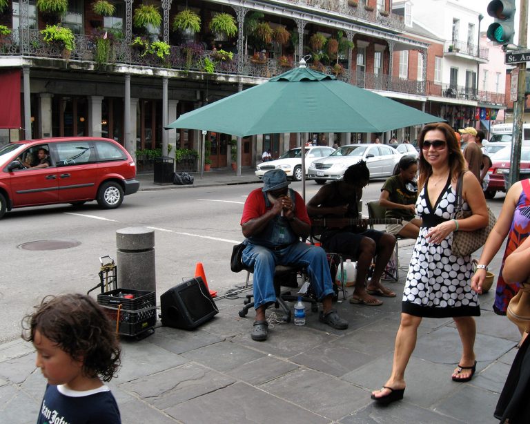 A group of musicians playing on the street in front of Cafe du Monde under an umbrella