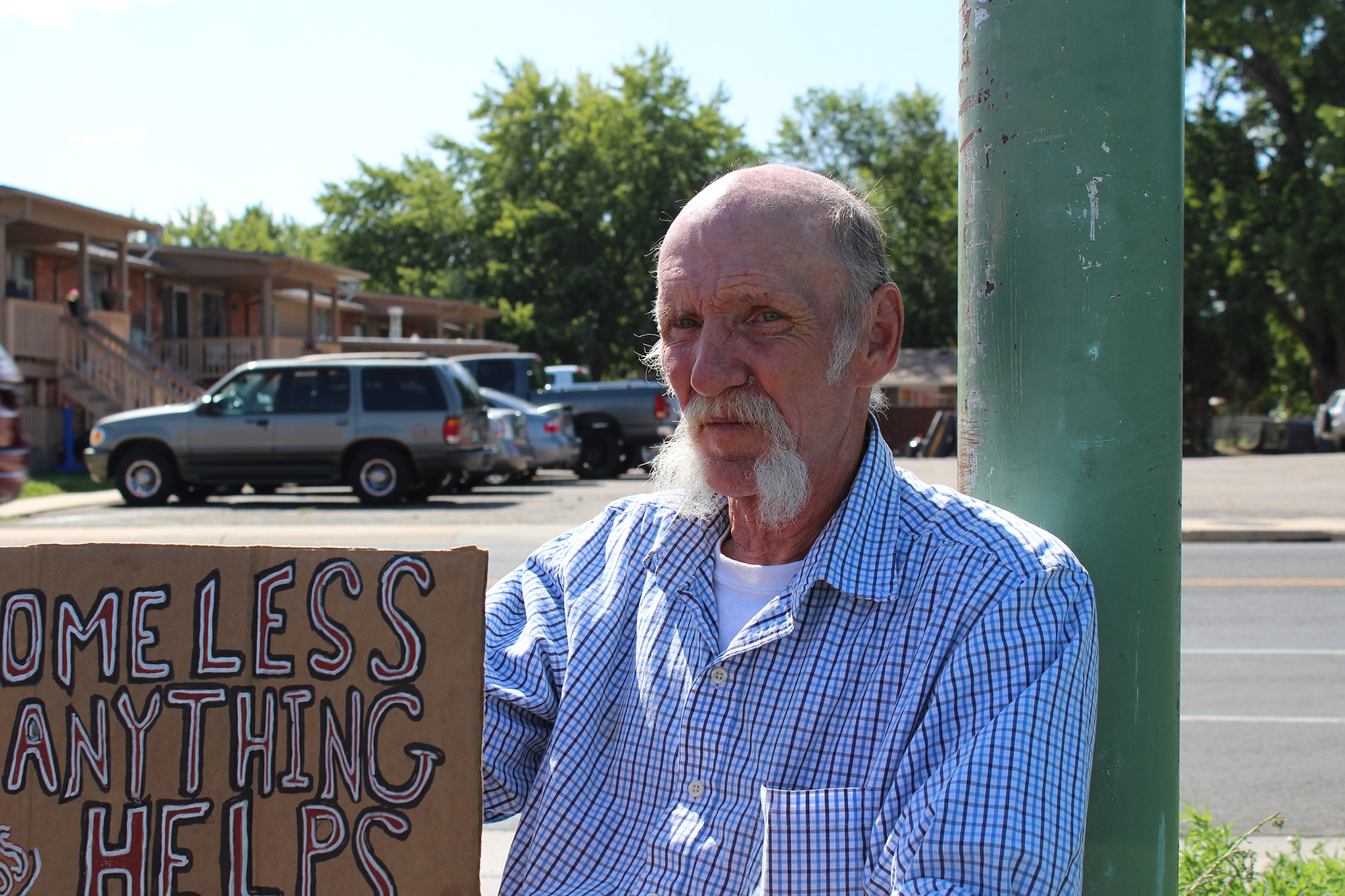 Homeless man holding a sign by a lamppost